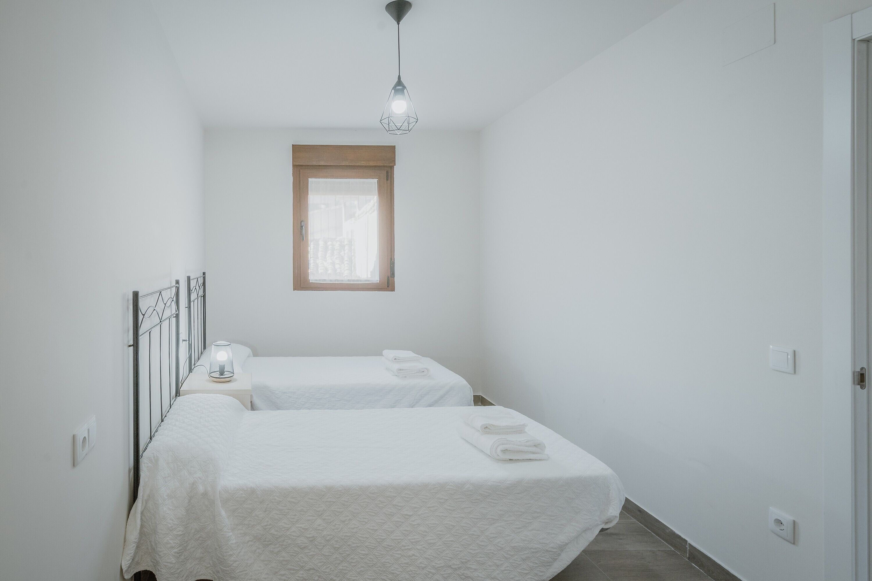 Une petite pièce propre, avec deux lits, une fenêtre et un luminaire suspendu.