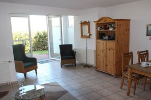 Ein Zimmer mit Esstisch, zwei Stühlen, einem Schrank, einer Stehlampe und einem Glastisch mit Weingläsern.