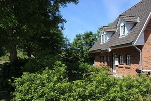 Ein zweigeschossiges Backsteinhhaus mit geneigtem Dach, Gauben und einer kleinen Veranda.