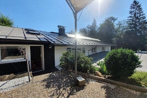 A modern house with a solar panel roof, a covered outdoor area, and a gravel driveway. - Watzmann holiday apartment for couples (Schönau am Königssee)