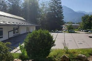A building with a parking lot, surrounded by trees and mountains in the background. - Watzmann holiday apartment for couples (Schönau am Königssee)