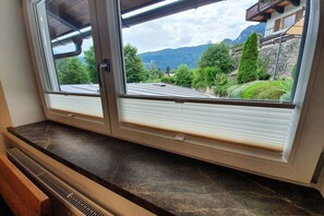 A window with a view of a mountainous landscape, a wooden bench, and a stone wall. - Watzmann holiday apartment for couples (Schönau am Königssee)