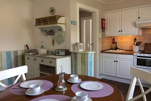 A kitchen with white cabinets, a stove, and a dining table set with white plates and cups. - Holiday apartment in Sylt with swimming pool (Sylt)