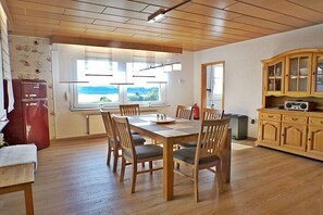 A dining area with a wooden table and chairs, a kitchen with wooden cabinets, and a view through the window. - Holiday home with lake view (Driedorf)