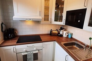 A kitchen with white cabinets, a black microwave, a toaster, and a sink. - Holiday home with lake view (Driedorf)