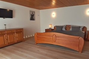 A bedroom with a wooden bed, a TV mounted on the wall, and a bedside table with a lamp. - Holiday home with lake view (Driedorf)
