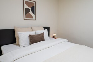 Een net opgemaakt bed met een zwart hoofdbord, witte en bruine kussens, en een klein nachtkastje met een lamp.