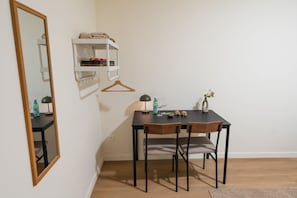 Et lille rum med et skrivebord, to stole, et spejl, en hylde med bøger, en flaske og en vase.