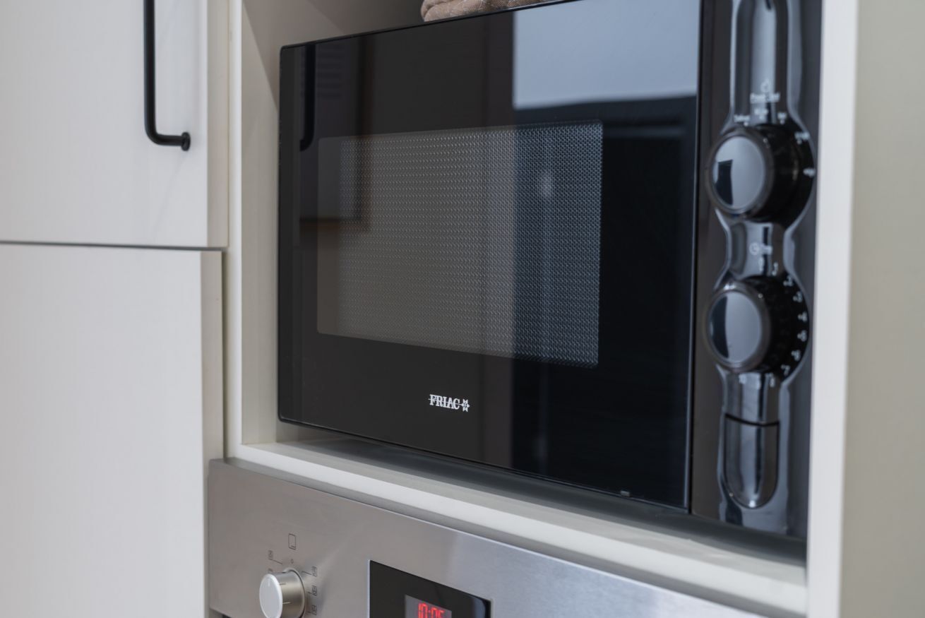 Een zwarte magnetron met een digitaal display, een bedieningsknop en een merknaam die op de voorkant zichtbaar is.