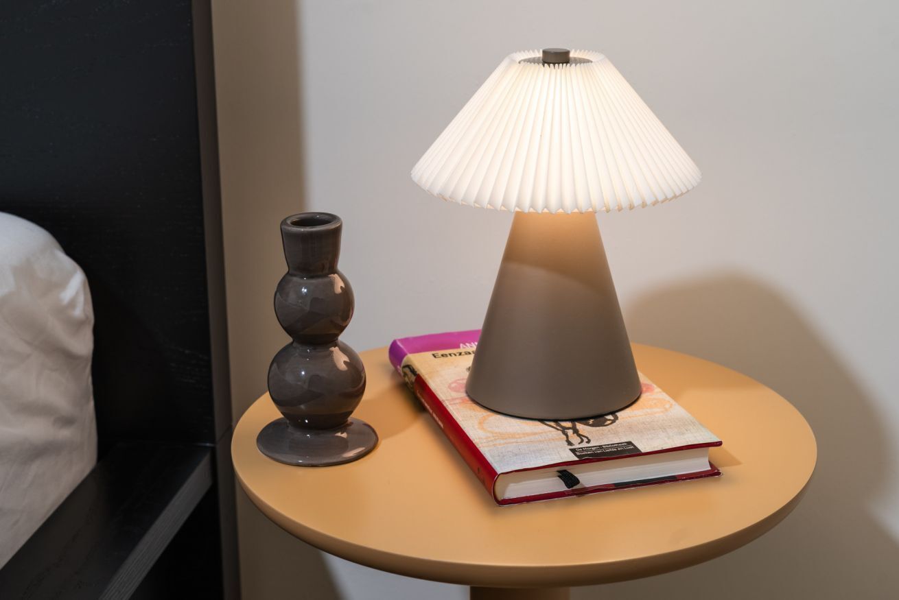 Een nachtkastje met een lamp, een vaas en een boek.