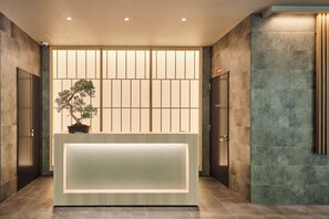 A reception desk with a potted bonsai tree, a sliding door, and a wall with a vertical wooden panel. - NICO HOTEL Osaka Namba (Osaka)
