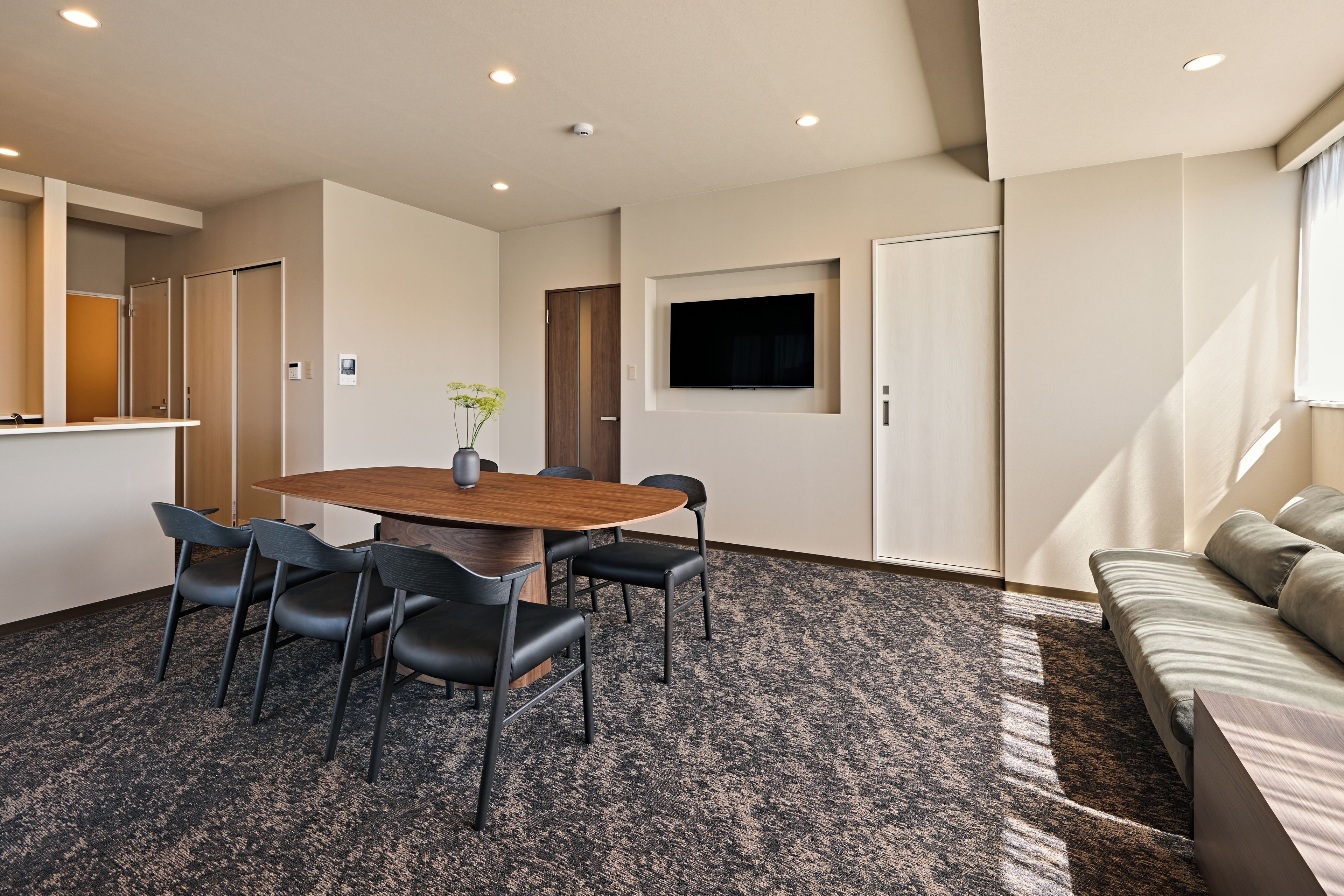 A conference room with a round table, six chairs, a small plant, a flat-screen TV, and a sofa with cushions.