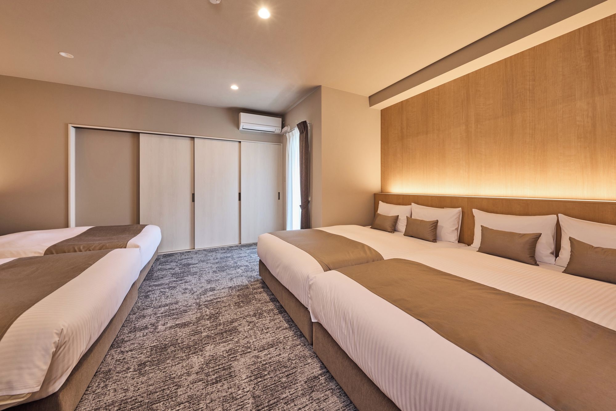 Une chambre d’hôtel avec deux lits, une grande fenêtre, une armoire et un appareil de climatisation.
