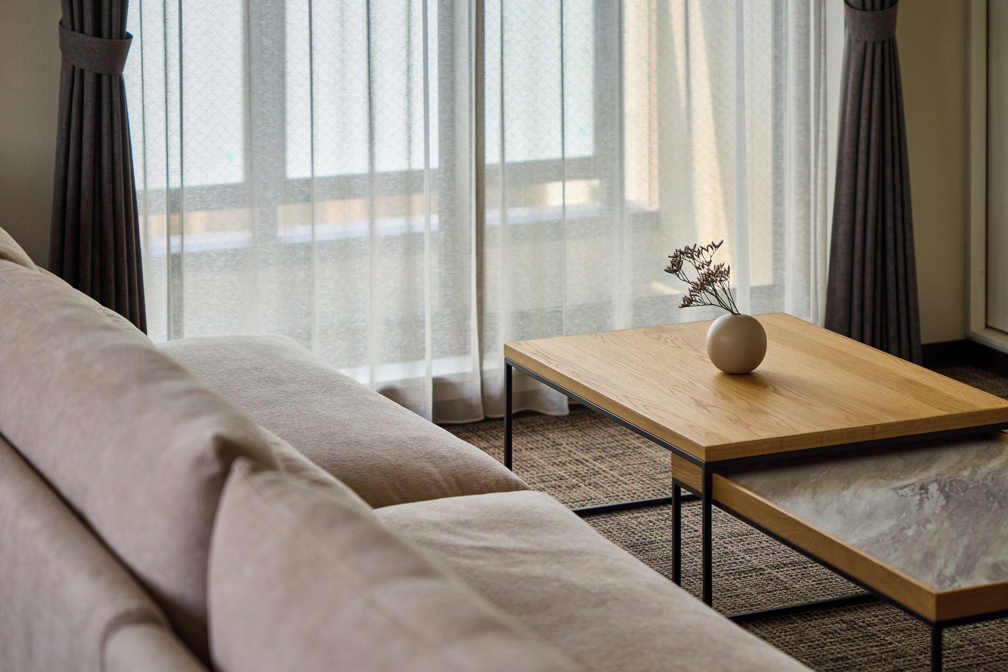 A modern living room with a sofa, a wooden coffee table, and sheer curtains.