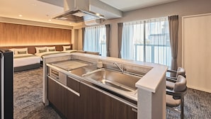 Ett modernt hotellrum med ett litet kök, ett stort fönster med gardiner, en säng med kuddar och ett golv täckt av matta.