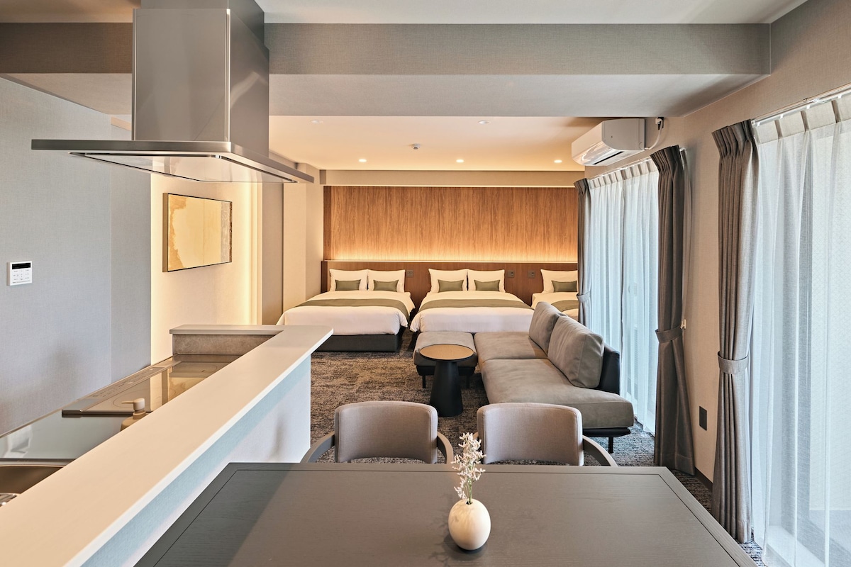 A hotel room with a bed, a sofa, a dining table, and a small side table.