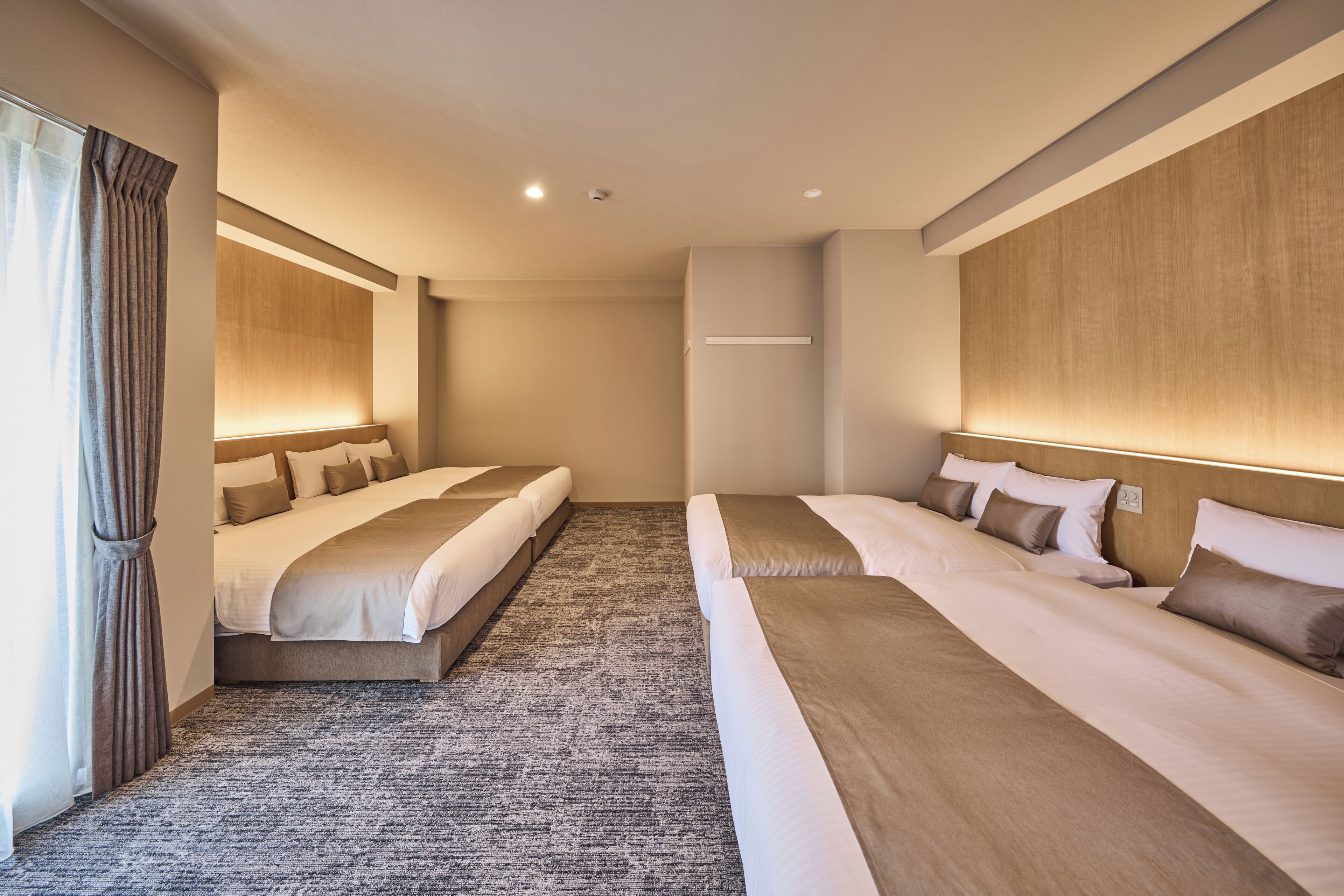 A hotel room with two beds, a carpeted floor, and a large window with curtains.