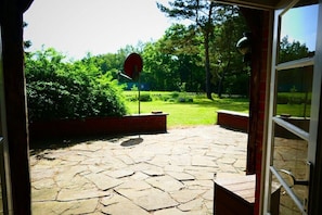 An outdoor patio with stone flooring, a red circular sign, and a view of a well-maintained lawn and trees. - Holiday home in Essel with swimming pool (Essel)