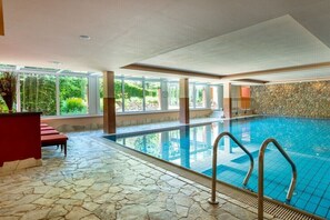 An indoor swimming pool with stone flooring, clear glass walls, and a stone wall. - Holiday home in Essel with swimming pool (Essel)