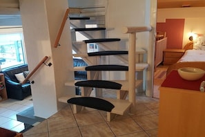 A spiral staircase with black cushioned steps, a wooden handrail, and a white wall. - Holiday home with 3 bedrooms (Frielendorf)