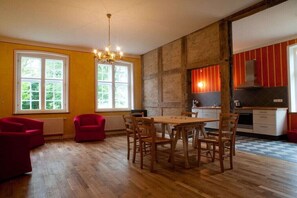 Ein Essbereich mit Holztisch und -stühlen, einer Kristallleuchter und einer Küche im Hintergrund.