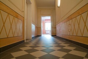 Ein Korridor mit Schachbrettfußboden, Holzvertäfelung mit geometrischen Mustern und einer Tür zu einem weiteren Raum.