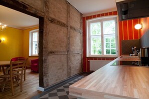 Eine Küche mit einer Holzausziehtheke, einer roten und gelben Wand sowie einem Fenster mit Blick auf Grünflächen.