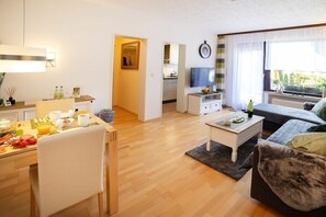 Ein modernes Wohnzimmer mit Essbereich, Fernseher und einer Küche im Hintergrund.