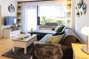Ein Wohnzimmer mit einer Couch, einem Couchtisch, einem Fernseher und einem Fenster mit Vorhängen.