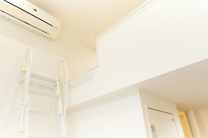 Eine weiße Klimaanlage an der Wand montiert, eine weiße Leiter, die an der Wand lehnt, und eine teilweise sichtbare Tür.