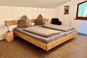 Ein Schlafzimmer mit einem hölzernen Bett, zwei Kissen, einem Nachttisch, einer Lampe, einem Sessel und einem Bild einer Kuh an der Wand.