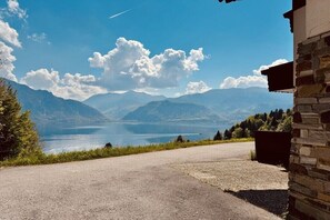 Ein gepflasterter Weg führt zu einem Steinhaus mit Blick auf einen See und Berge.