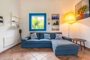 Ein Wohnzimmer mit einem blauen Sofa, einer Lampe, einem kleinen Tisch und einem Fenster mit blauem Rahmen.