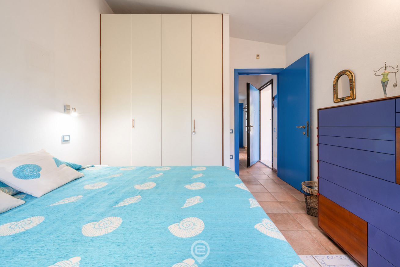 A bedroom with a bed, a wardrobe, and a door leading to another room.