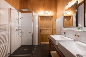 Ein modernes Badezimmer mit einer Duschkabine, zwei Waschbecken und einer Holztür.
