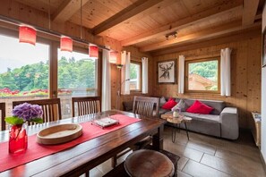 Ein Holzblockbau-Innenraum mit Esstisch, Sofa und großen Fenstern mit Blick auf einen Garten.