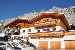 Ein mehrstöckiges Holzchalet mit Balkonen, einer Garage und verschneiter Landschaft.