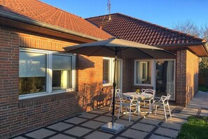 Ein Backsteinhaus mit Ziegeldach, eine Terrasse mit Tisch und Stühlen sowie ein überdachter Außenbereich zum Sitzen.