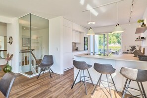 Eine moderne Küche mit Glastrennwand, Barhocker und Pendelleuchten.
