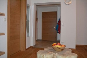 Ein Zimmer mit Holzboden, einer Holztür, einem Spiegel, einer Uhr und einer Obstschale auf einem Baumstumpf.