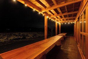 A wooden deck with benches, string lights, and a stone wall in the background.