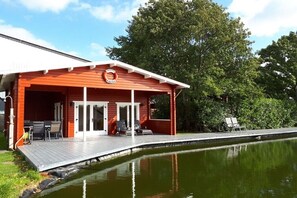 Ein Holzhaus mit überdachter Terrasse, Pool und Gartenmöbeln.
