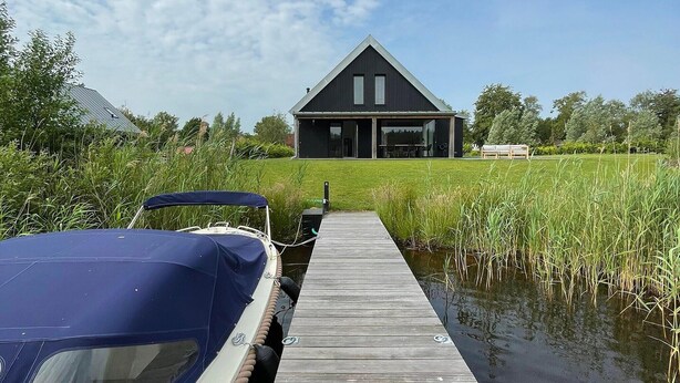 Een huis met een groot terras dat leidt naar een steiger waar een boot is afgemeerd.