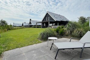 Ein modernes Haus mit großem Rasen, Sitzgelegenheiten im Freien und einem Metall-Dach.