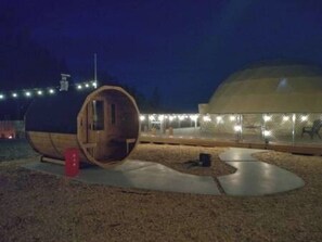 Un edificio esférico con revestimiento de madera, una gran estructura cilíndrica y un área cercada con luces.