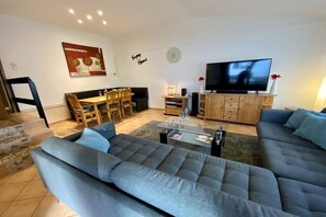 Ein modernes Wohnzimmer mit einer Sofagarnitur, einem Esstisch und einem Flachbildfernseher.