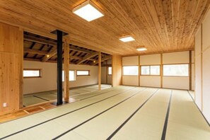 A tatami mat room with wooden beams, tatami flooring, and large windows.