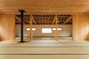 Una habitación con esteras de tatami, vigas de madera, un pilar negro y ventanas.