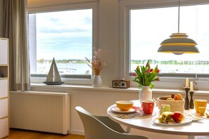 Ein Essbereich mit einem für das Frühstück gedeckten Tisch, Blick auf das Wasser und einem Radio auf der Fensterbank.