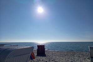Ein Strand mit blauem Himmel, strahlender Sonne und einer Reihe weißer Liegestühle.